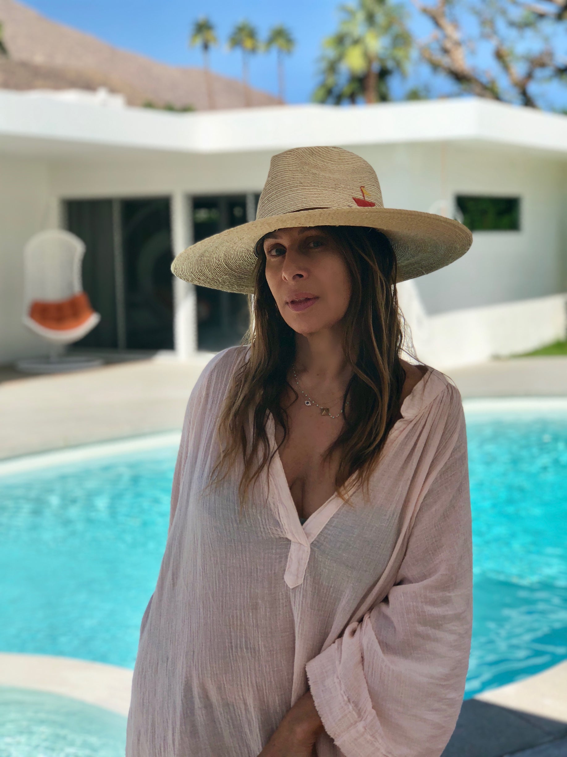 A photo of Temma Dahan-Newman poolside in her own 9seed loungewear pink top and a sin hat.