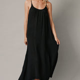 The full body front photo of a beautiful blonde woman wearing a TULUM black maxi dress in a lightweight gauze. She is standing on a grey canvas.