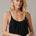 The close up front photo of a beautiful blonde woman wearing a TULUM black maxi dress in a lightweight gauze. She is standing on a grey canvas.
