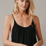 The close up front photo of a beautiful blonde woman wearing a TULUM black maxi dress in a lightweight gauze. She is standing on a grey canvas.