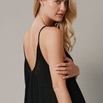 The close up back angled photo of a beautiful blonde woman wearing a TULUM black maxi dress in a lightweight gauze. She is standing on a grey canvas.